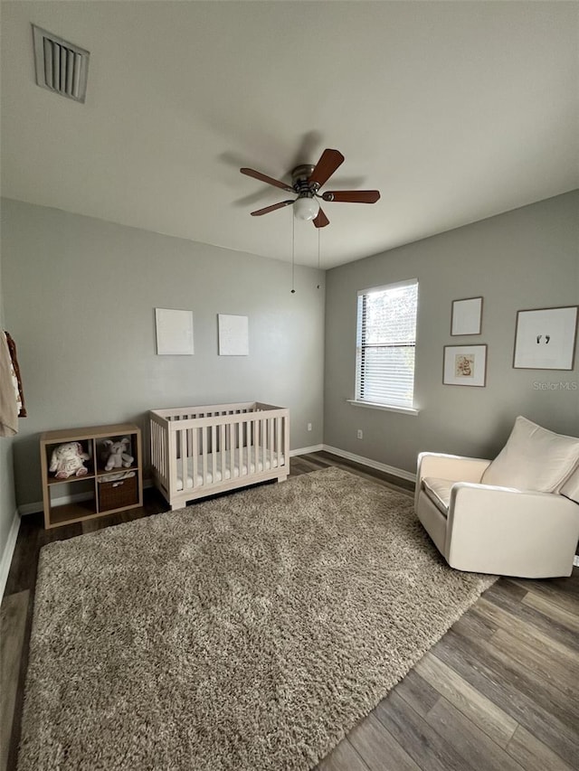 bedroom featuring ceiling fan, a nursery area, and dark wood-type flooring