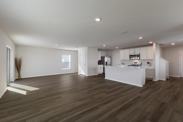 kitchen with white cabinets, dark hardwood / wood-style flooring, stainless steel appliances, and a kitchen island with sink