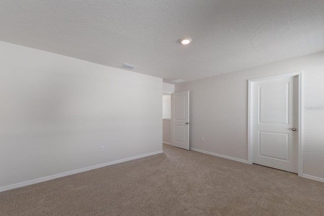 spare room featuring light colored carpet and a textured ceiling