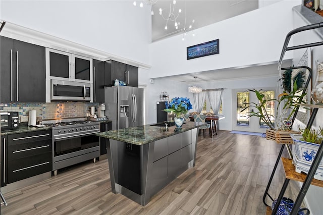 kitchen with a towering ceiling, backsplash, stainless steel appliances, a chandelier, and a kitchen island