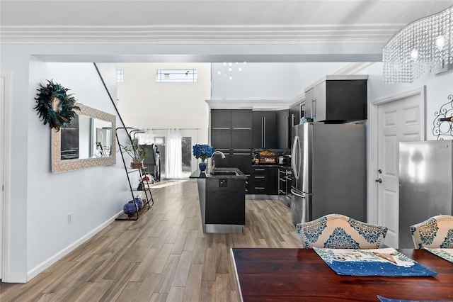 kitchen with stainless steel fridge, sink, a chandelier, light hardwood / wood-style floors, and an island with sink