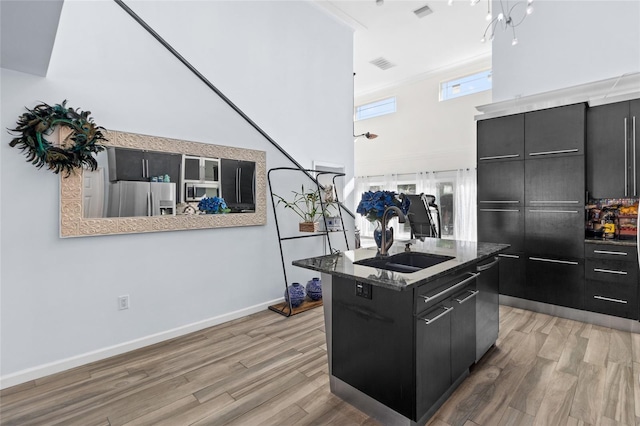 kitchen with sink, light wood-type flooring, an island with sink, appliances with stainless steel finishes, and ornamental molding