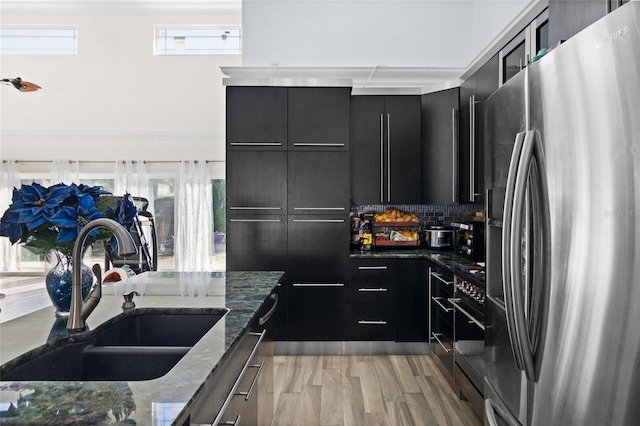 kitchen with decorative backsplash, dark stone counters, sink, stainless steel fridge with ice dispenser, and light hardwood / wood-style floors