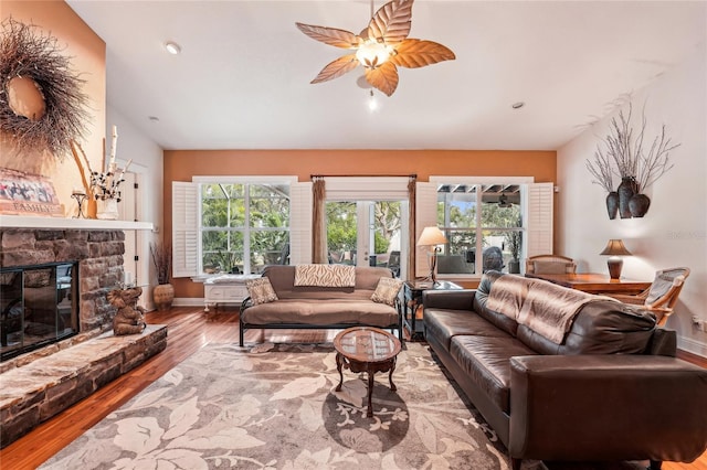 living room with hardwood / wood-style flooring, a stone fireplace, ceiling fan, and vaulted ceiling