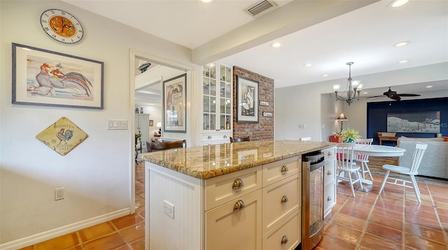 kitchen with wine cooler, light stone counters, pendant lighting, a kitchen island, and ceiling fan with notable chandelier