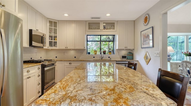 kitchen featuring backsplash, stainless steel appliances, light stone counters, and a breakfast bar area