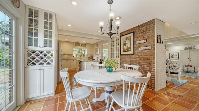 tiled dining space with a notable chandelier, a wealth of natural light, sink, and brick wall