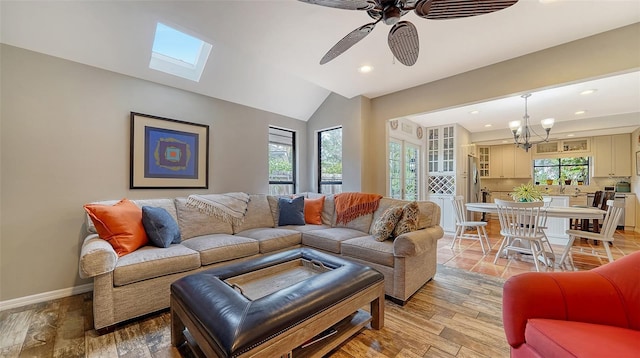 living room with ceiling fan with notable chandelier, light hardwood / wood-style floors, and lofted ceiling with skylight