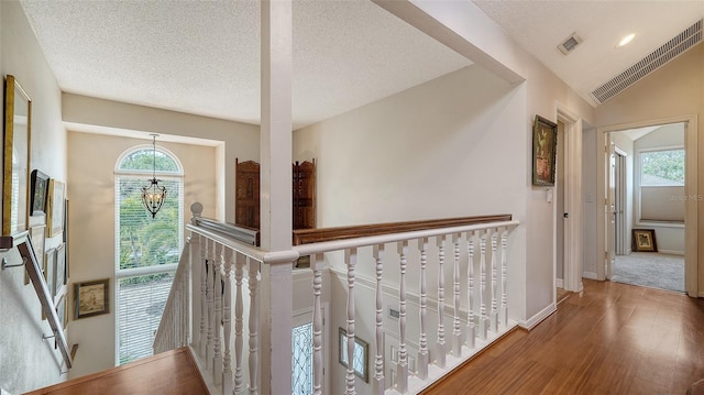 hall featuring a chandelier, a textured ceiling, hardwood / wood-style flooring, and lofted ceiling