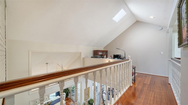 hall featuring hardwood / wood-style flooring, lofted ceiling with skylight, and a textured ceiling