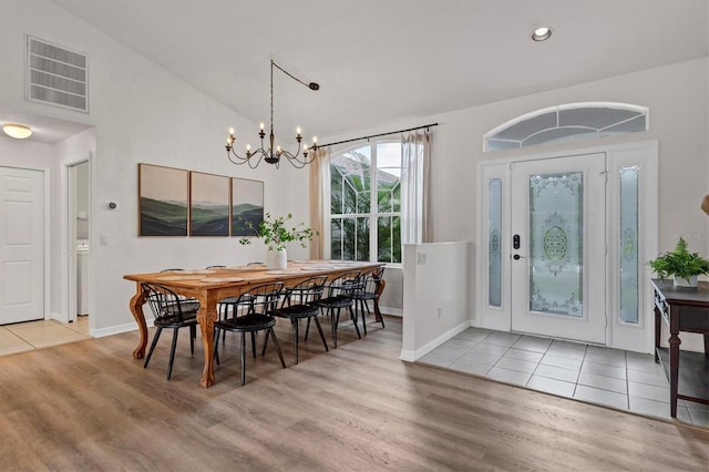 dining room with an inviting chandelier, washer / dryer, light wood-type flooring, and vaulted ceiling