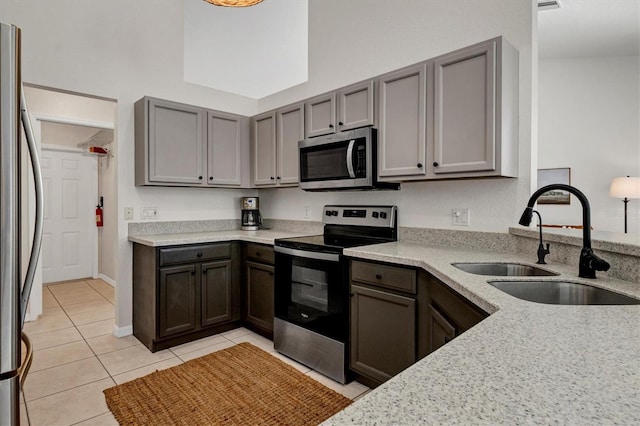 kitchen with sink, stainless steel appliances, light stone counters, gray cabinets, and light tile patterned floors