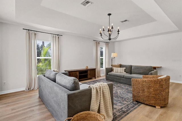 living room with a tray ceiling, an inviting chandelier, and light hardwood / wood-style flooring