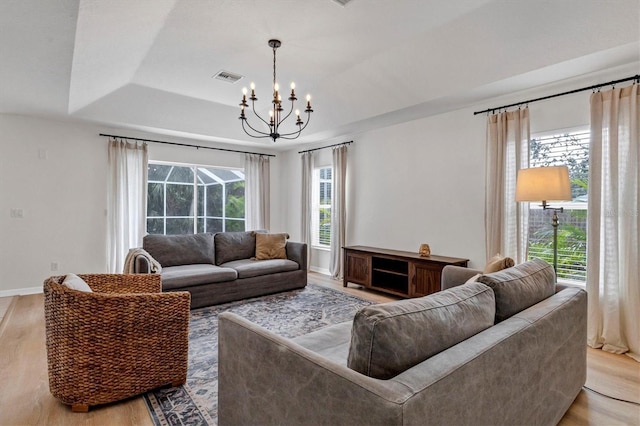 living room with light wood-type flooring, a raised ceiling, and a notable chandelier