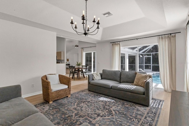 living room with a tray ceiling, an inviting chandelier, and light hardwood / wood-style flooring