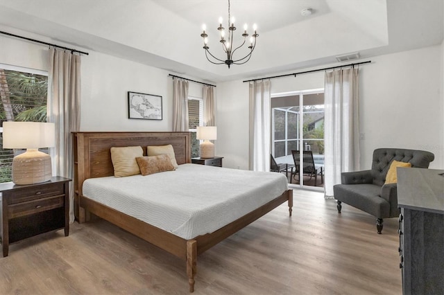 bedroom featuring access to exterior, a tray ceiling, an inviting chandelier, and multiple windows