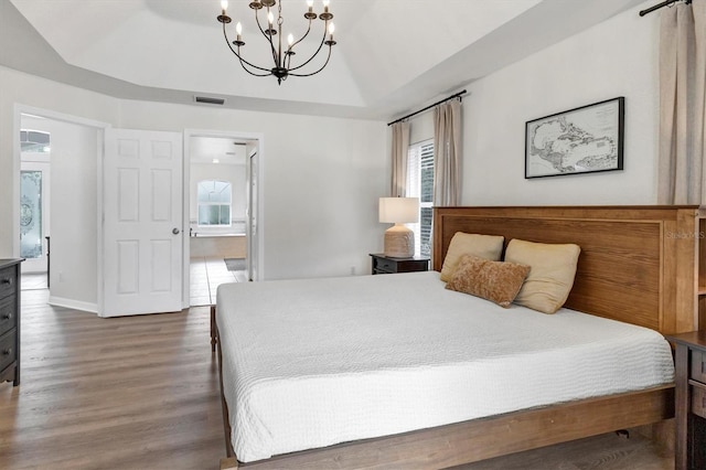 bedroom with a notable chandelier, dark wood-type flooring, a tray ceiling, and ensuite bath