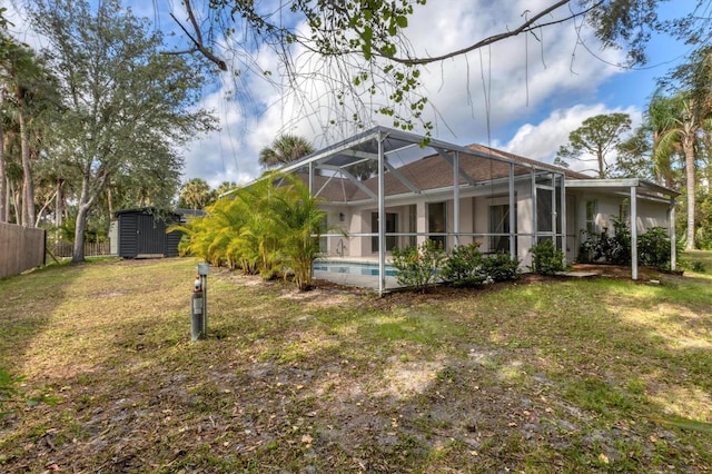 rear view of property with a yard, glass enclosure, and a storage unit