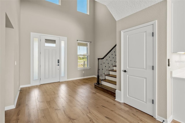 foyer with light hardwood / wood-style flooring, a textured ceiling, and a towering ceiling