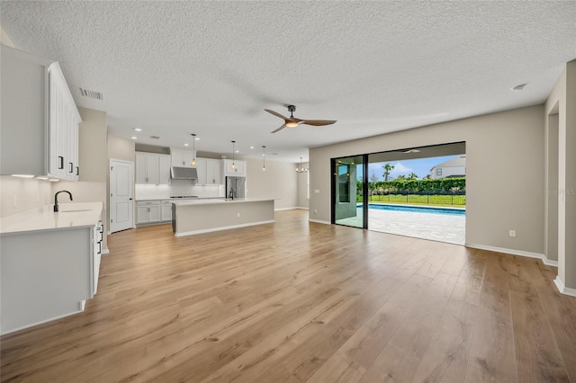 unfurnished living room featuring ceiling fan, light hardwood / wood-style flooring, sink, and a textured ceiling