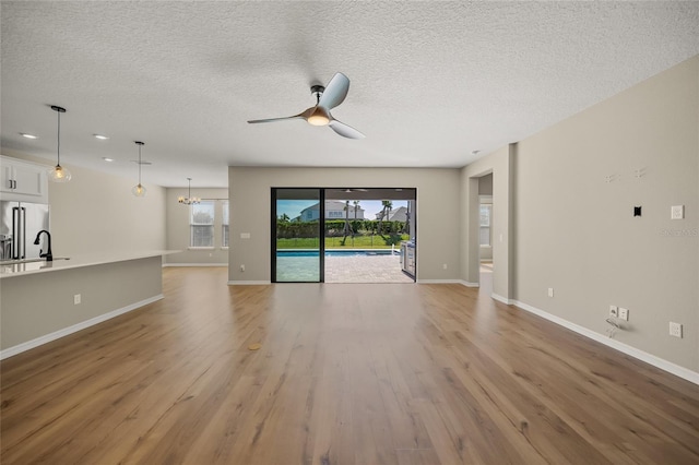 unfurnished living room featuring ceiling fan with notable chandelier, light wood-type flooring, and a textured ceiling