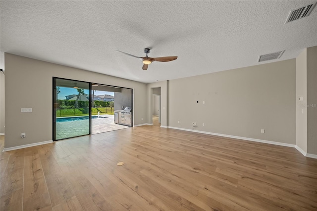 empty room with ceiling fan, light wood-type flooring, and a textured ceiling