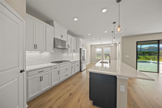 kitchen with a center island with sink, sink, pendant lighting, stainless steel appliances, and white cabinets