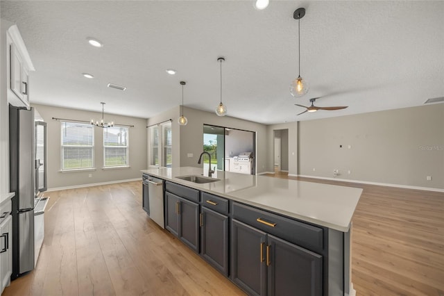 kitchen with appliances with stainless steel finishes, light hardwood / wood-style flooring, an island with sink, decorative light fixtures, and sink