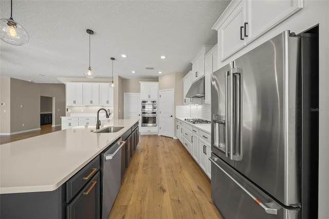 kitchen with a center island with sink, appliances with stainless steel finishes, sink, pendant lighting, and white cabinets