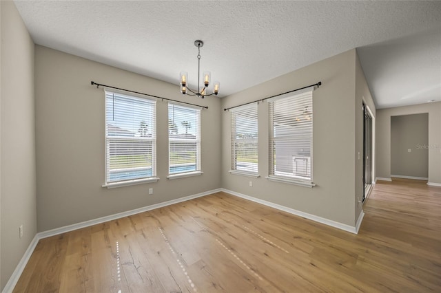 spare room featuring an inviting chandelier, light hardwood / wood-style flooring, and a textured ceiling