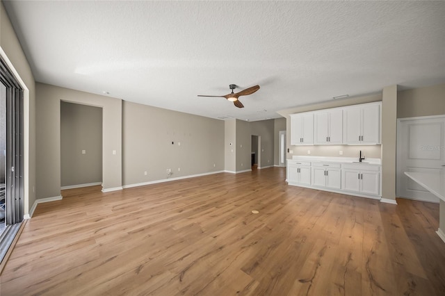 unfurnished living room featuring light hardwood / wood-style flooring, ceiling fan, a textured ceiling, and sink