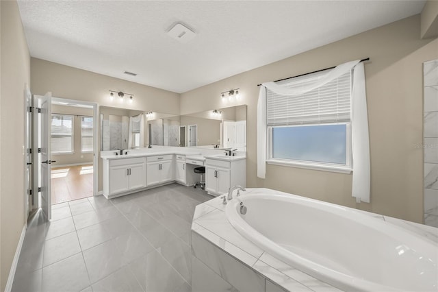 bathroom with a textured ceiling, tiled bath, vanity, and tile patterned flooring