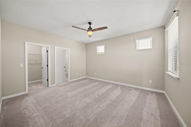 unfurnished bedroom with a spacious closet, a textured ceiling, connected bathroom, ceiling fan, and light colored carpet