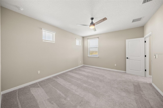 spare room with a textured ceiling, light colored carpet, and ceiling fan