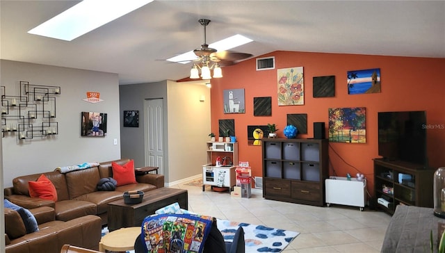 living room with vaulted ceiling with skylight, ceiling fan, and light tile patterned floors