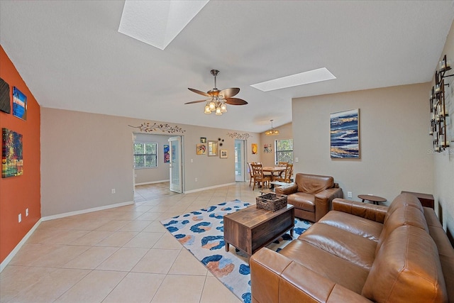 living room featuring ceiling fan, vaulted ceiling with skylight, a wealth of natural light, and light tile patterned floors