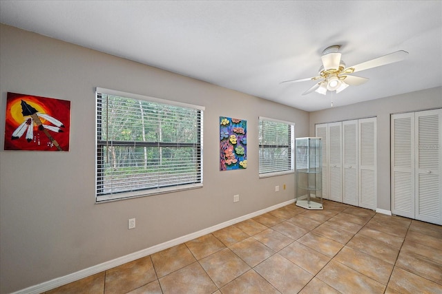 unfurnished bedroom with ceiling fan, light tile patterned floors, and multiple closets