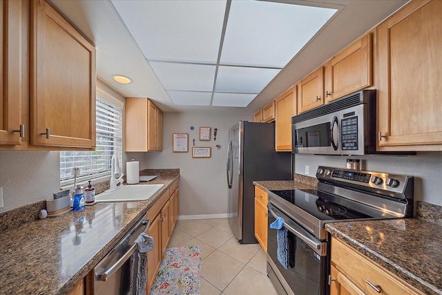 kitchen with appliances with stainless steel finishes, light brown cabinetry, light tile patterned floors, sink, and dark stone countertops