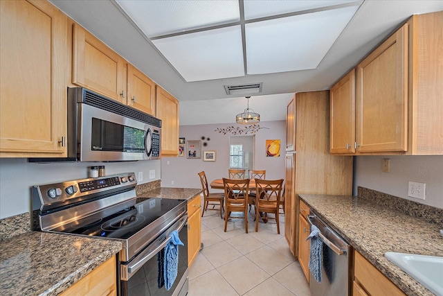 kitchen with appliances with stainless steel finishes, hanging light fixtures, light brown cabinetry, and dark stone countertops