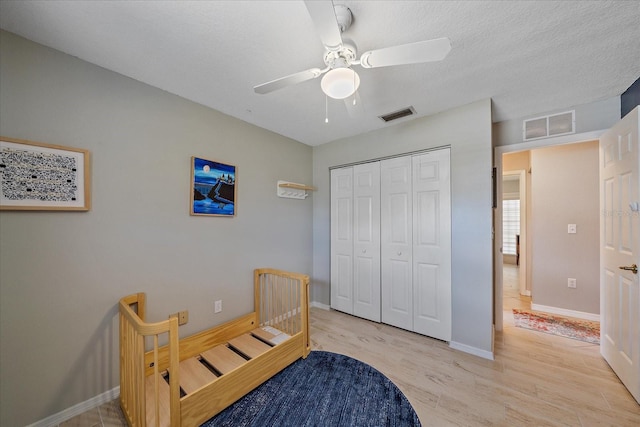 bedroom with ceiling fan, light hardwood / wood-style floors, a textured ceiling, and a closet