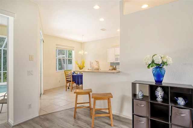 kitchen featuring kitchen peninsula, light hardwood / wood-style flooring, white cabinets, a chandelier, and hanging light fixtures