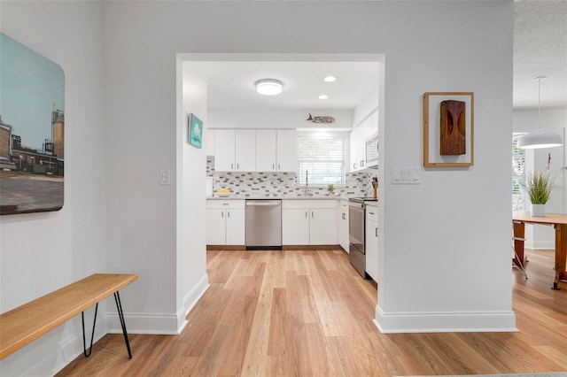 kitchen featuring appliances with stainless steel finishes, light wood-type flooring, tasteful backsplash, sink, and white cabinetry