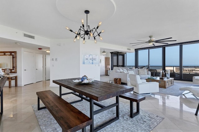 tiled dining room with ceiling fan with notable chandelier, a water view, and a wall of windows