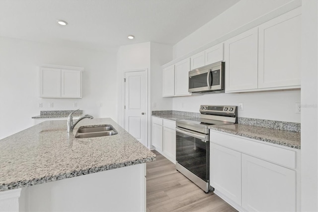 kitchen with white cabinets, a center island with sink, sink, light wood-type flooring, and stainless steel appliances