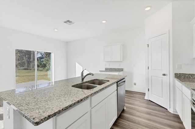 kitchen with appliances with stainless steel finishes, light stone counters, a kitchen island with sink, sink, and white cabinetry