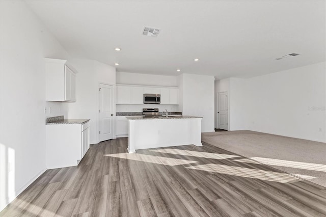 kitchen featuring stainless steel appliances, a center island with sink, light hardwood / wood-style flooring, stone counters, and white cabinets