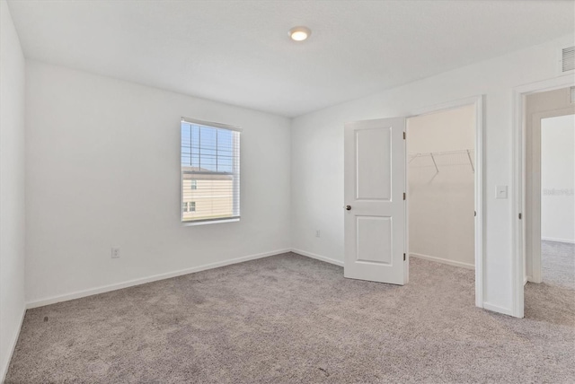 unfurnished bedroom with a walk in closet, light carpet, and a closet