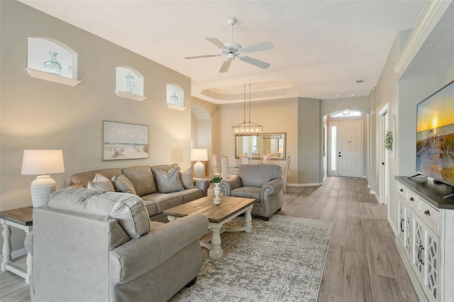 living room featuring ceiling fan with notable chandelier, light wood-type flooring, and a tray ceiling