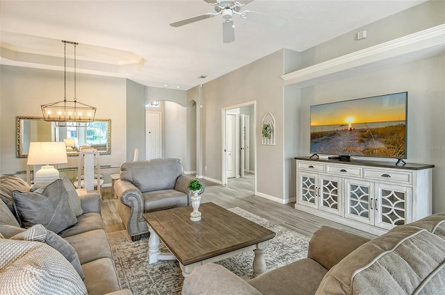 living room with ceiling fan with notable chandelier, light wood-type flooring, and a tray ceiling