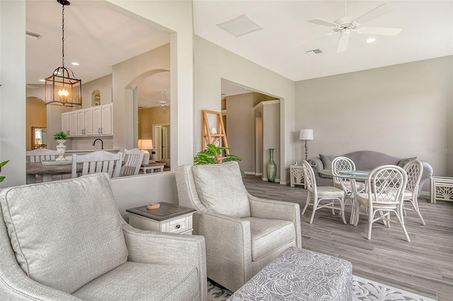 living room featuring ceiling fan with notable chandelier and light wood-type flooring